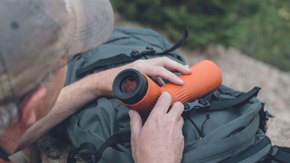 Birdwatcher checking optics beside a backpack